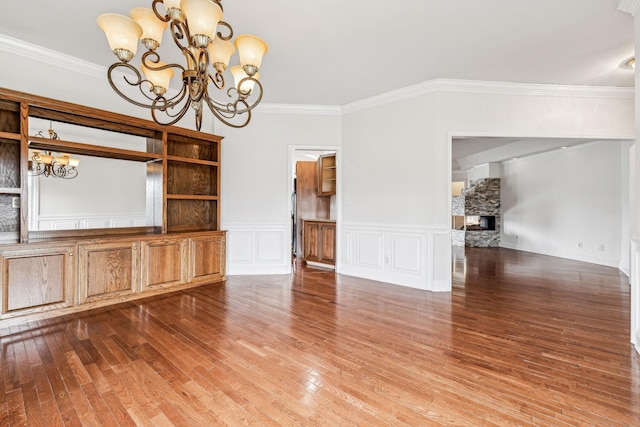 interior space with ornamental molding, wood finished floors, a stone fireplace, an inviting chandelier, and a decorative wall