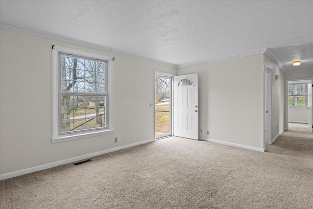 carpeted spare room with visible vents, a textured ceiling, baseboards, and ornamental molding
