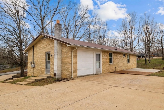 view of property exterior featuring brick siding, a garage, driveway, and a chimney
