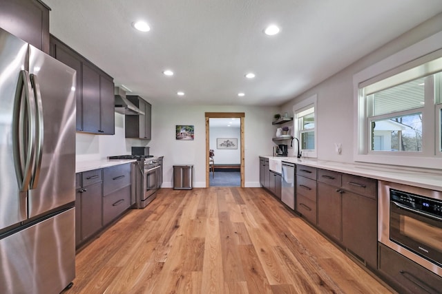 kitchen featuring light wood-style flooring, recessed lighting, appliances with stainless steel finishes, wall chimney range hood, and light countertops
