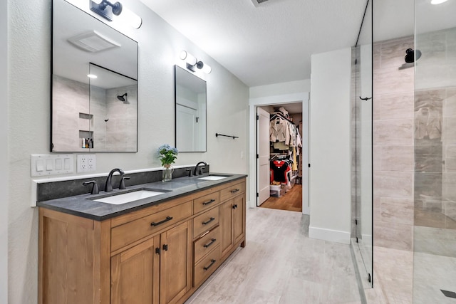 bathroom featuring double vanity, a stall shower, wood finished floors, and a sink