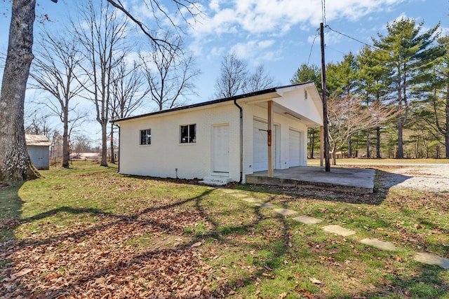 exterior space featuring a detached garage, brick siding, an outbuilding, and a lawn