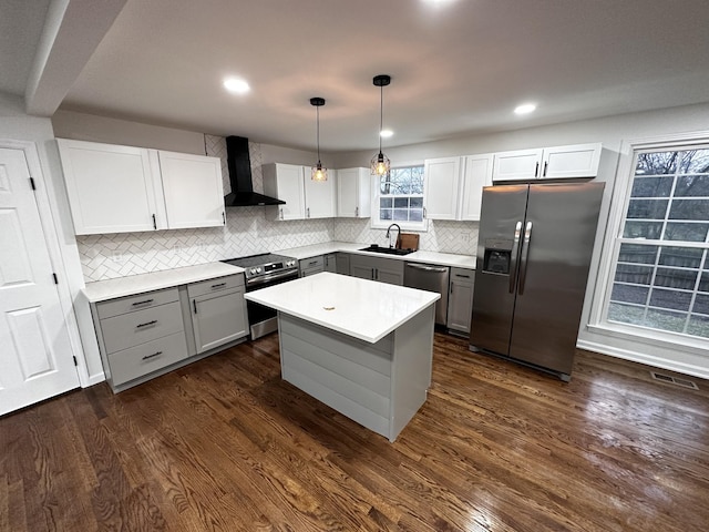 kitchen with gray cabinetry, a sink, dark wood-style floors, appliances with stainless steel finishes, and wall chimney exhaust hood