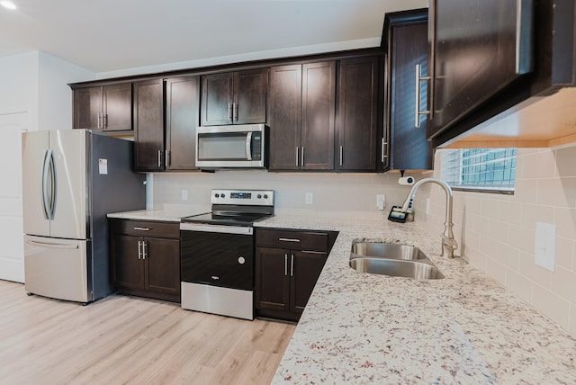 kitchen with dark brown cabinets, light stone counters, light wood-style flooring, appliances with stainless steel finishes, and a sink