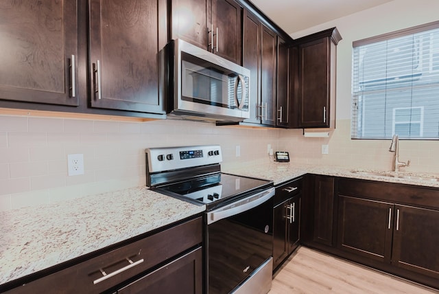 kitchen with light stone counters, appliances with stainless steel finishes, light wood-style floors, and a sink