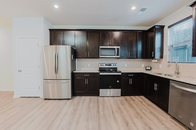 kitchen with a sink, light stone counters, light wood-style floors, and appliances with stainless steel finishes