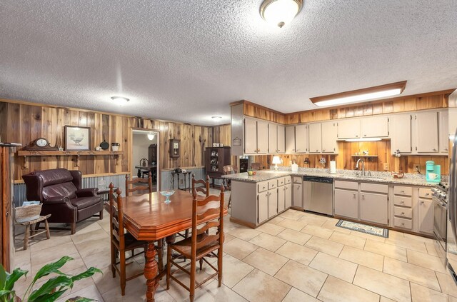 kitchen with light stone countertops, wood walls, dishwasher, a textured ceiling, and a sink