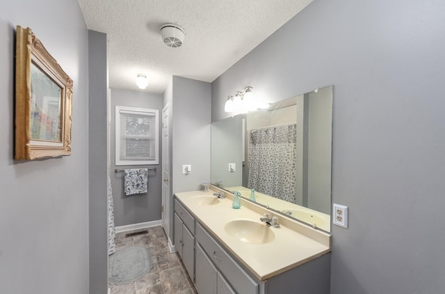 bathroom featuring double vanity, a textured ceiling, baseboards, and a sink