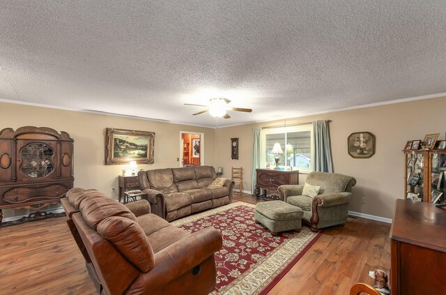 living area featuring baseboards, ceiling fan, ornamental molding, wood finished floors, and a textured ceiling