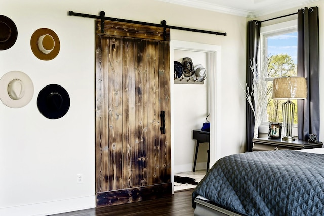 bedroom featuring a closet, baseboards, ornamental molding, a barn door, and wood finished floors