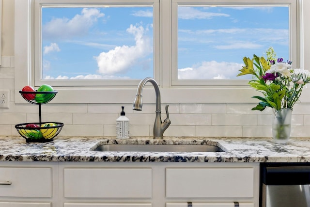 kitchen featuring white cabinets, tasteful backsplash, light stone countertops, and a sink