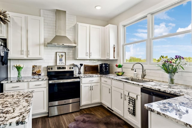 kitchen featuring wall chimney range hood, white cabinets, a sink, and appliances with stainless steel finishes