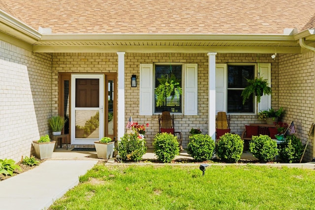 entrance to property with a porch, a lawn, a shingled roof, and brick siding