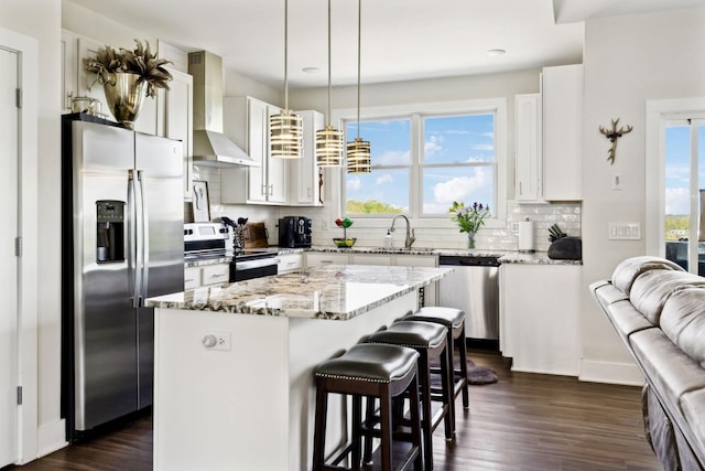 kitchen with tasteful backsplash, a sink, wall chimney range hood, stainless steel appliances, and a kitchen island