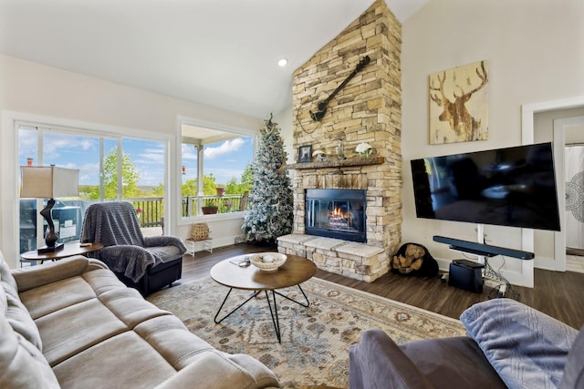 living room with high vaulted ceiling, a stone fireplace, baseboards, and wood finished floors