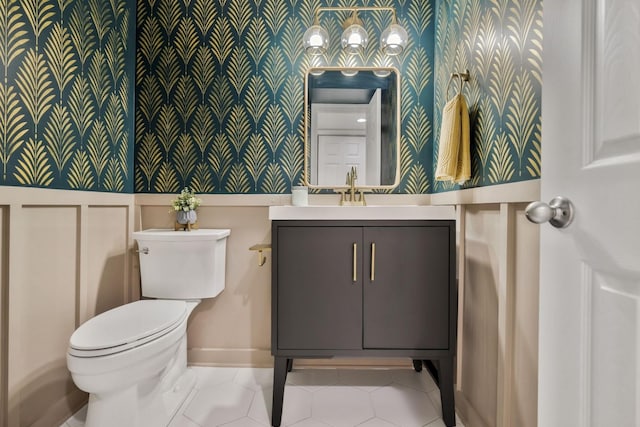 half bath with tile patterned floors, toilet, wallpapered walls, baseboards, and vanity