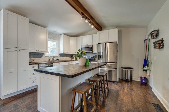 kitchen with tasteful backsplash, vaulted ceiling with beams, a breakfast bar, white cabinets, and stainless steel appliances