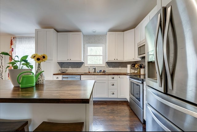 kitchen with a sink, stainless steel appliances, butcher block countertops, and white cabinetry