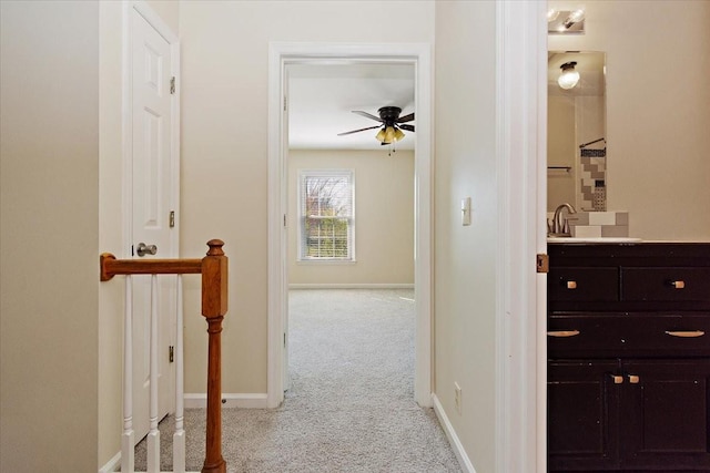 hallway featuring carpet, baseboards, and a sink