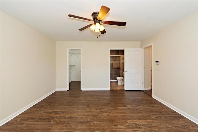 unfurnished bedroom with a walk in closet, baseboards, a closet, dark wood-style floors, and ensuite bath