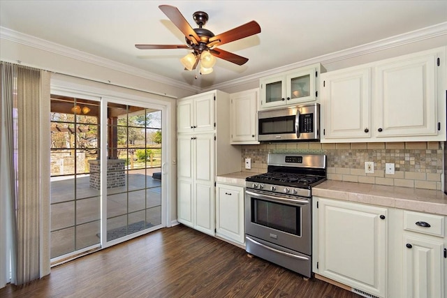 kitchen featuring a ceiling fan, dark wood finished floors, ornamental molding, stainless steel appliances, and tasteful backsplash