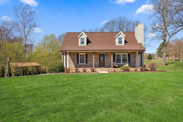 new england style home with brick siding, covered porch, a chimney, and a front yard