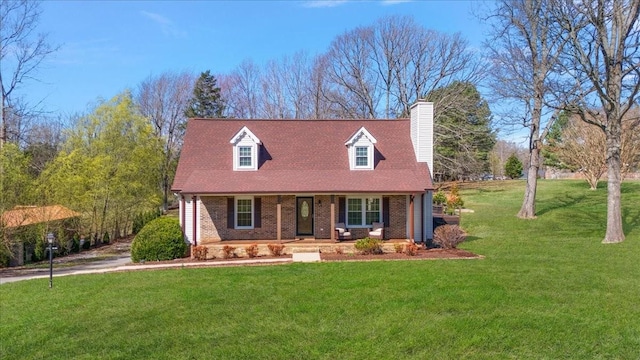 new england style home featuring a front lawn, covered porch, brick siding, and a chimney