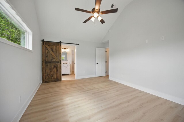 unfurnished bedroom with visible vents, a barn door, high vaulted ceiling, baseboards, and light wood-style floors