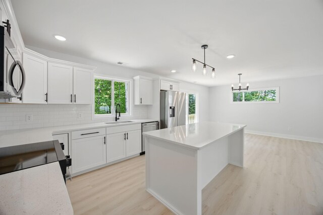 kitchen with appliances with stainless steel finishes, a sink, plenty of natural light, light wood-type flooring, and tasteful backsplash