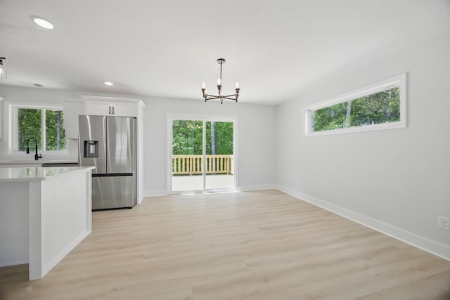 unfurnished dining area featuring an inviting chandelier, a sink, light wood-style floors, recessed lighting, and baseboards