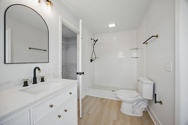 bathroom with a tile shower, a walk in closet, vanity, toilet, and wood finished floors
