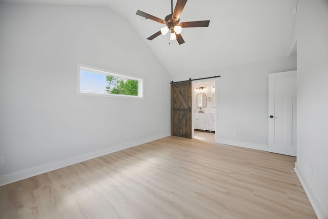 unfurnished bedroom with baseboards, light wood-type flooring, a barn door, and connected bathroom