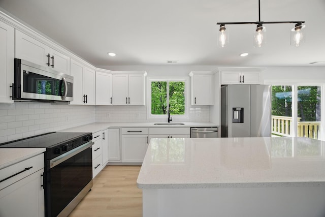 kitchen featuring a sink, light wood-style floors, stainless steel appliances, white cabinetry, and decorative backsplash