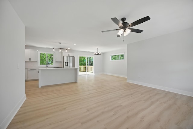 unfurnished living room featuring recessed lighting, baseboards, ceiling fan with notable chandelier, and light wood-type flooring