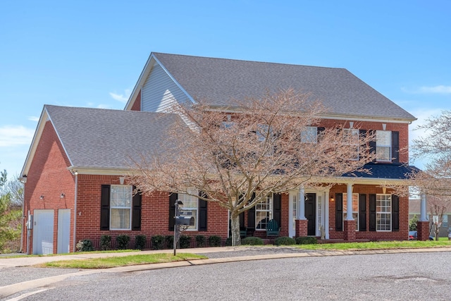 view of front of home with brick siding, covered porch, a garage, and roof with shingles