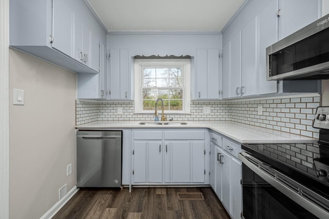 kitchen with light countertops, appliances with stainless steel finishes, dark wood-style floors, white cabinets, and a sink