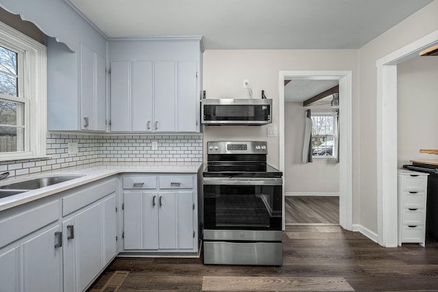 kitchen with baseboards, dark wood finished floors, stainless steel appliances, decorative backsplash, and light countertops