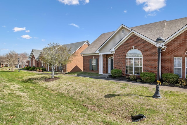 view of front of house featuring a front lawn, a shingled roof, and brick siding