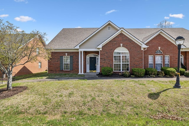 view of front of home featuring brick siding, a front yard, and roof with shingles
