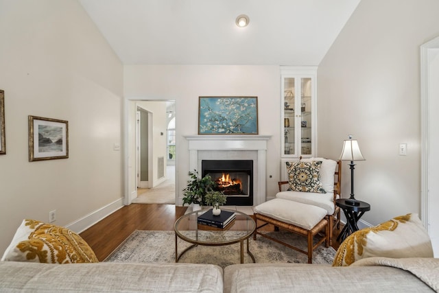 living area featuring a tiled fireplace, visible vents, baseboards, and wood finished floors