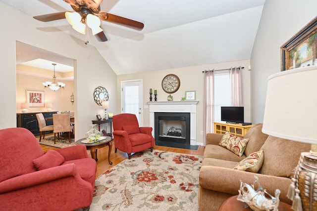 living room with vaulted ceiling, wood finished floors, a healthy amount of sunlight, and ceiling fan with notable chandelier