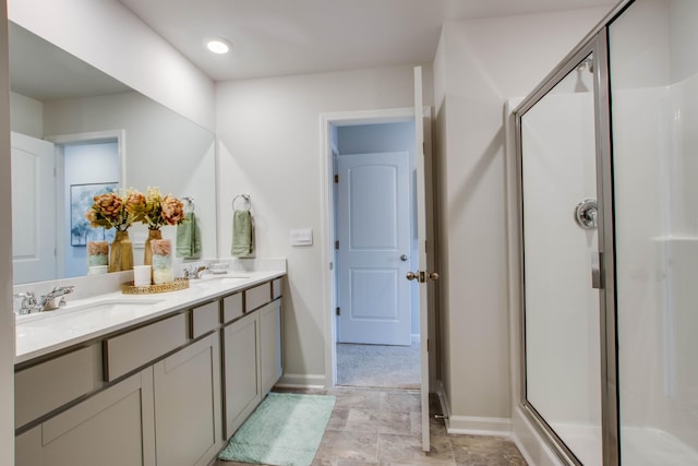 bathroom with double vanity, baseboards, a stall shower, and a sink