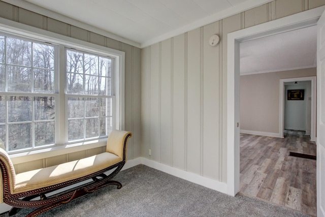 sitting room with a decorative wall, baseboards, and ornamental molding