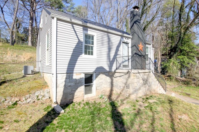 view of side of home featuring a lawn, central AC, a chimney, and fence