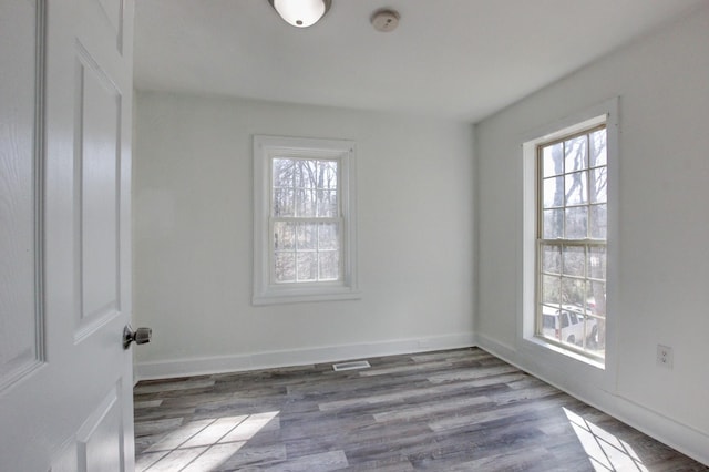unfurnished room with visible vents, a healthy amount of sunlight, baseboards, and wood finished floors