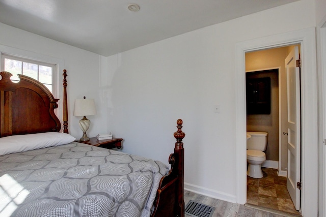 bedroom with visible vents, ensuite bathroom, baseboards, and wood finished floors