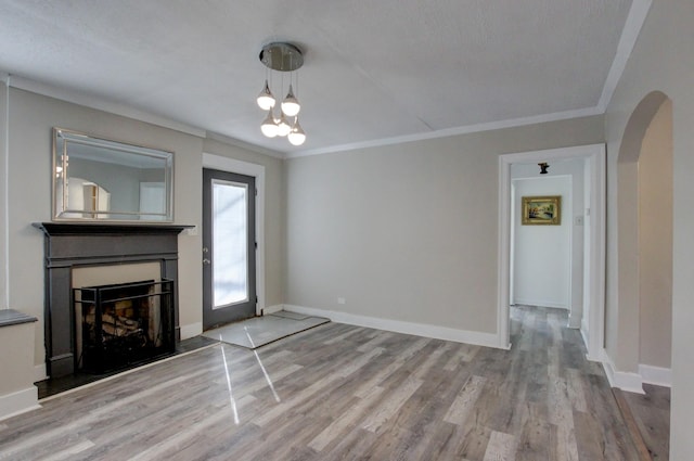 unfurnished living room featuring arched walkways, a fireplace, wood finished floors, and ornamental molding