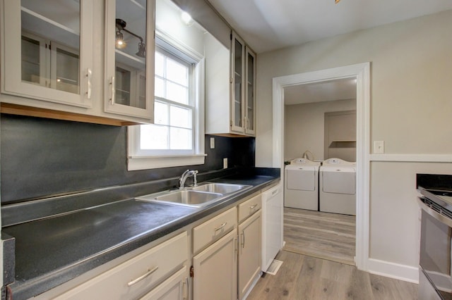 kitchen featuring a sink, dark countertops, separate washer and dryer, white dishwasher, and light wood finished floors
