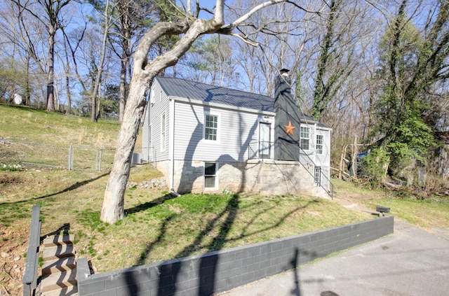 view of front facade featuring a front lawn, central AC, fence, metal roof, and a chimney