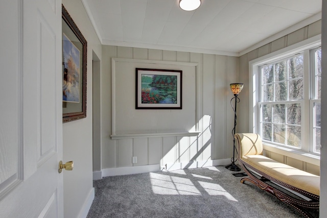 sitting room with carpet flooring, a decorative wall, baseboards, and ornamental molding